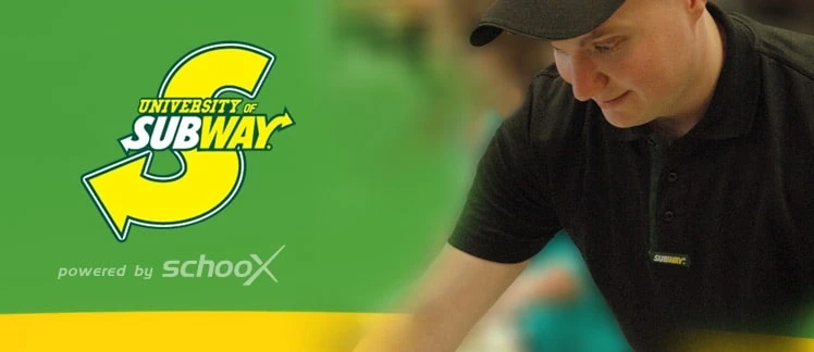A worker in a black Subway uniform prepares food with a green background featuring the Subway logo.