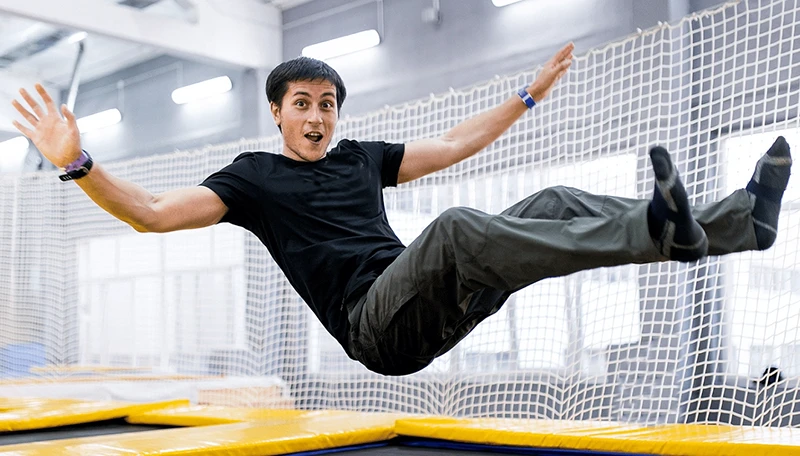 A man in a black shirt and gray pants jumping mid-air at a trampoline park.