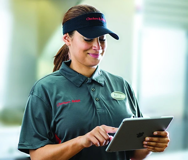 A woman wearing a visor and gray uniform, smiling while using a tablet.