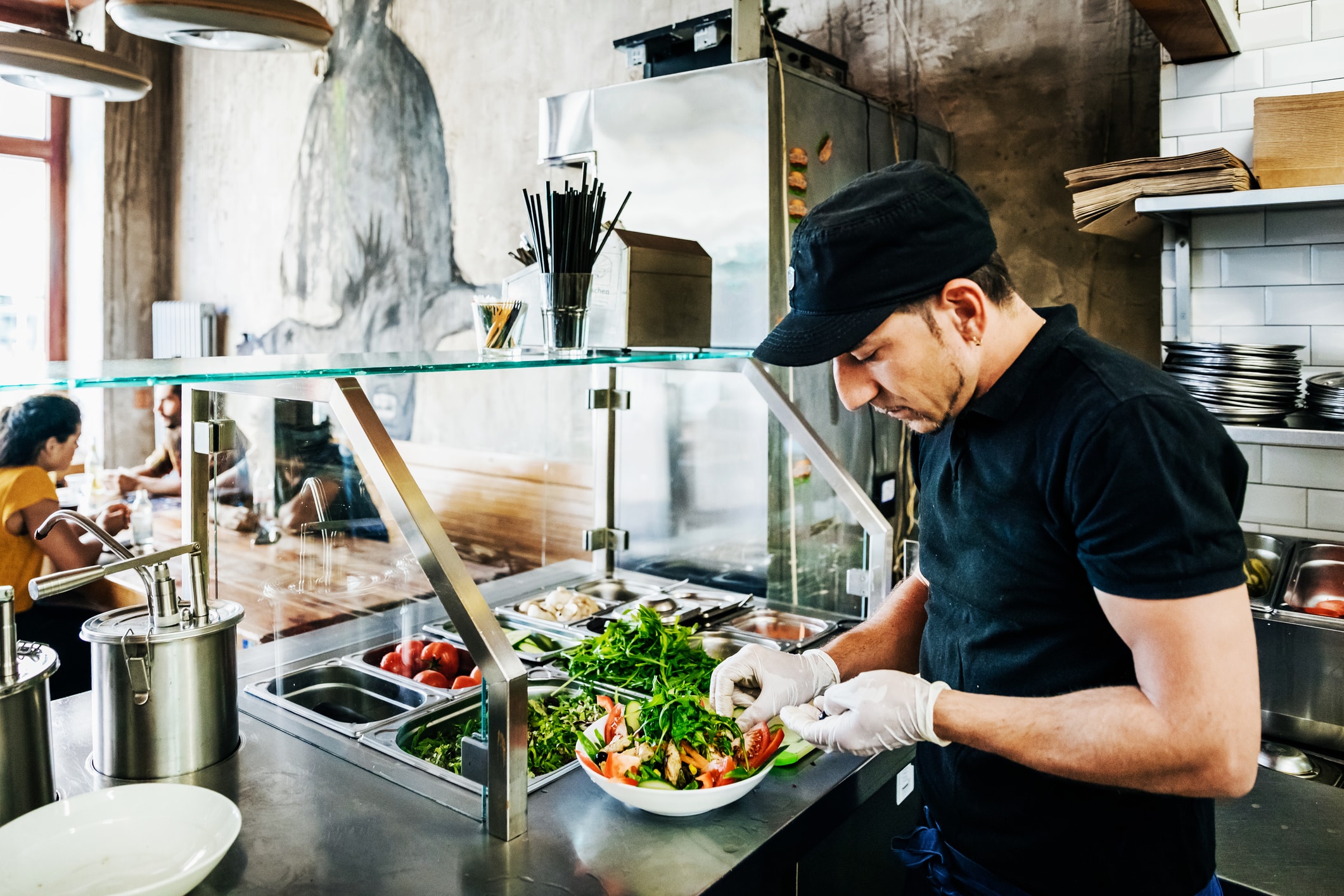 a chef preparing a salad dish for a customer in his trendy burger restaurant.