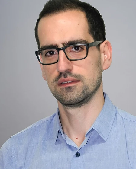 A man with glasses wearing a light blue shirt, looking directly at the camera.