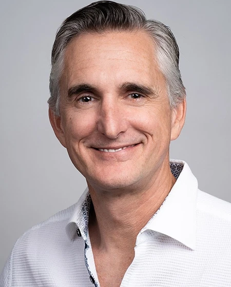 A smiling man with gray hair, wearing a white button-up shirt with a patterned collar.