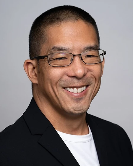 Man with short hair, wearing glasses and a black blazer, smiling at the camera.