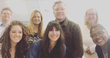 A group of seven people smiling for a photo in a bright office setting.