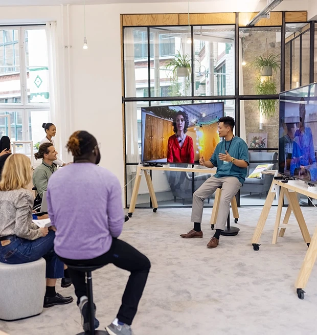 A group of people in a modern meeting space, actively participating in a presentation with screens.