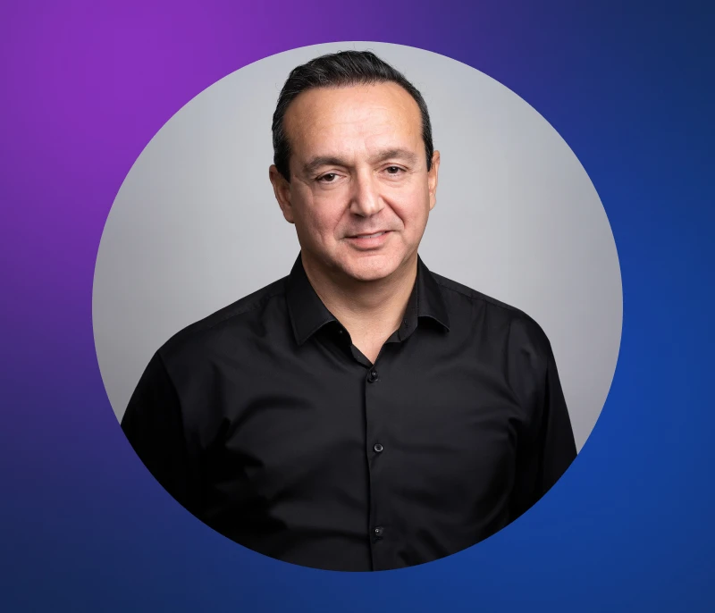 A man in a black shirt stands in front of a purple and blue circular background.