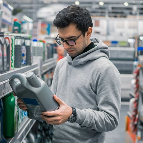 A person in a gray hoodie examines a gray oil container in an auto supply store aisle.