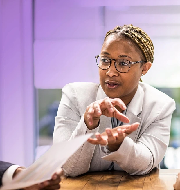 A woman in a gray suit talks while gesturing with her hands at a table.