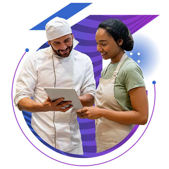 A chef in a white coat shows a tablet to a woman in a green shirt, both smiling.