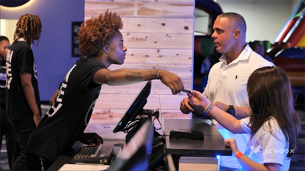 A young person hands a ticket to a man at a counter while a child is beside them.