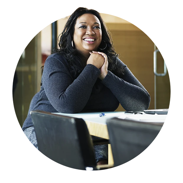 A smiling woman with long hair sitting at a table with a notebook and pen.