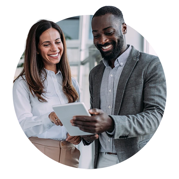 A woman and a man smiling while looking at a tablet together in an office setting.