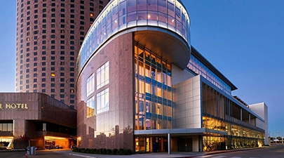 A modern hotel building with a curved glass exterior and bright lights at dusk.