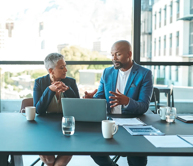 Two business professionals discussing ideas while reviewing information on a laptop