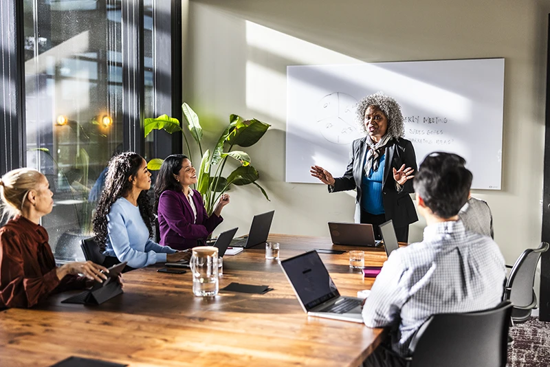 Business leader presenting to a team during a meeting with laptops at a conference table