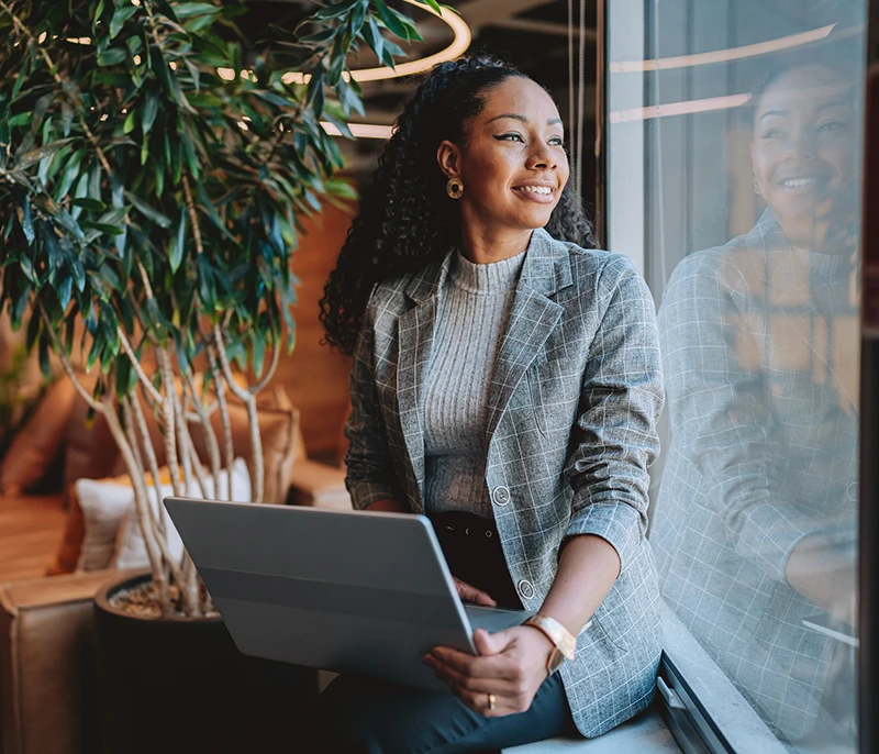 Business professional holding a laptop while looking out a window in a modern office