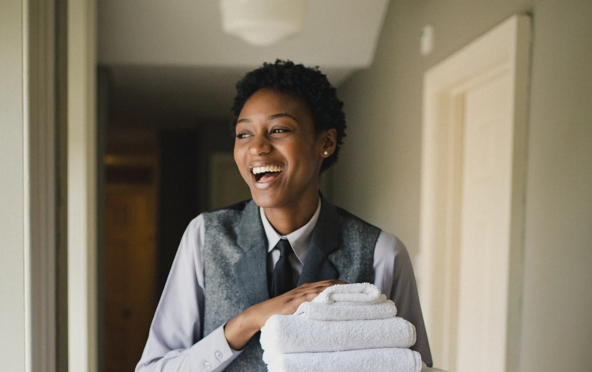 Hospitality employee holding folded towels in a hotel hallway