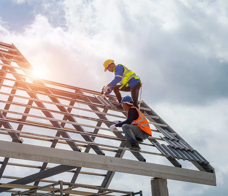 Construction workers installing a roof frame while wearing hard hats and high-visibility safety gear