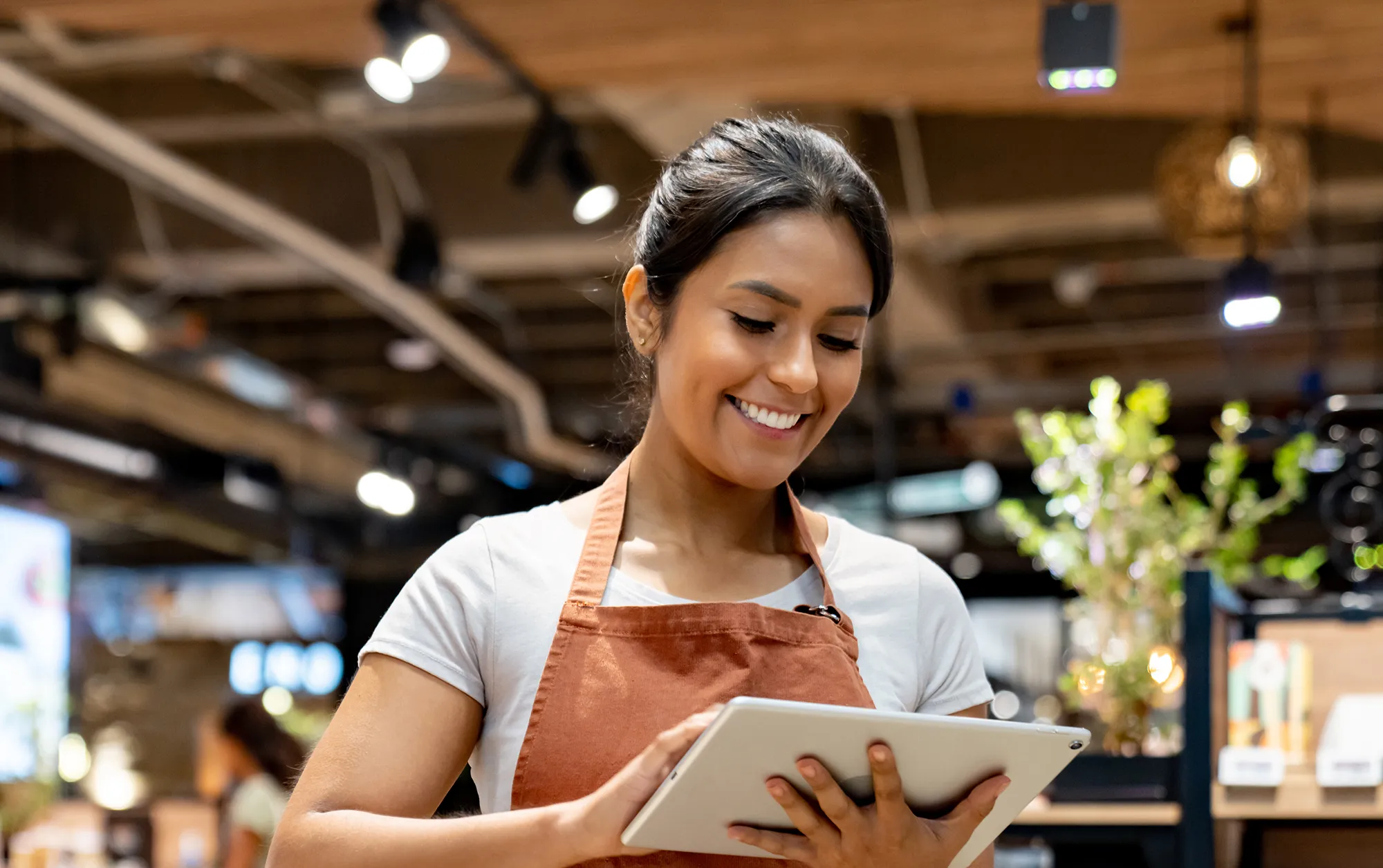 Smiling retail associate wearing an apron and using a tablet in a retail environment
