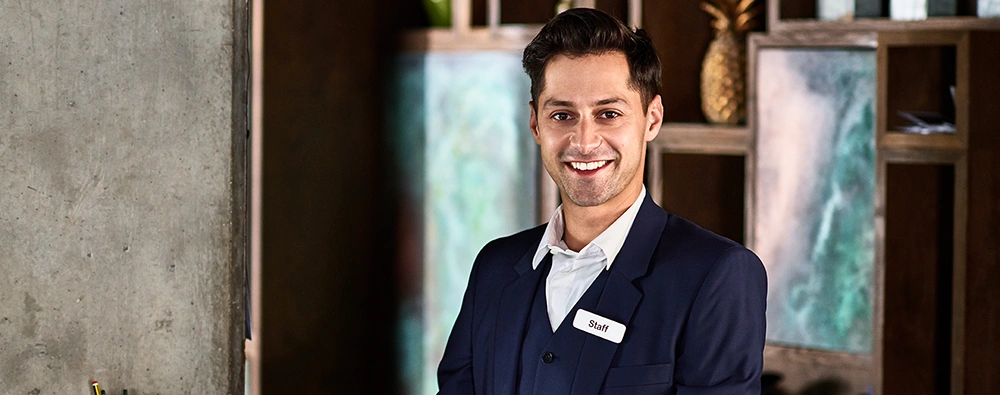 Hospitality employee wearing a staff badge and smiling at a hotel reception area