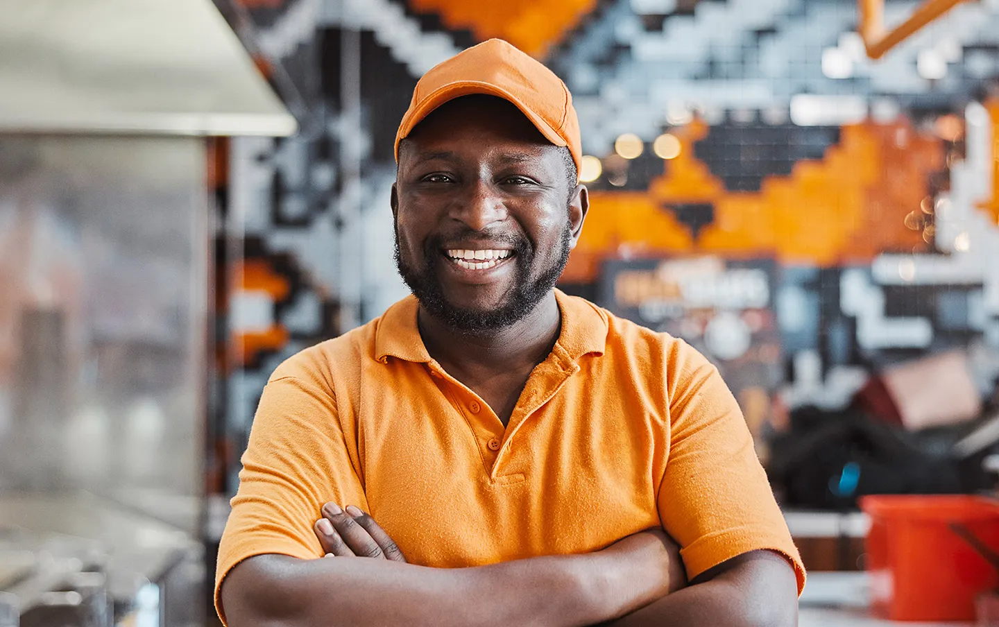 Smiling frontline restaurant employee wearing a uniform with arms crossed in a commercial kitchen