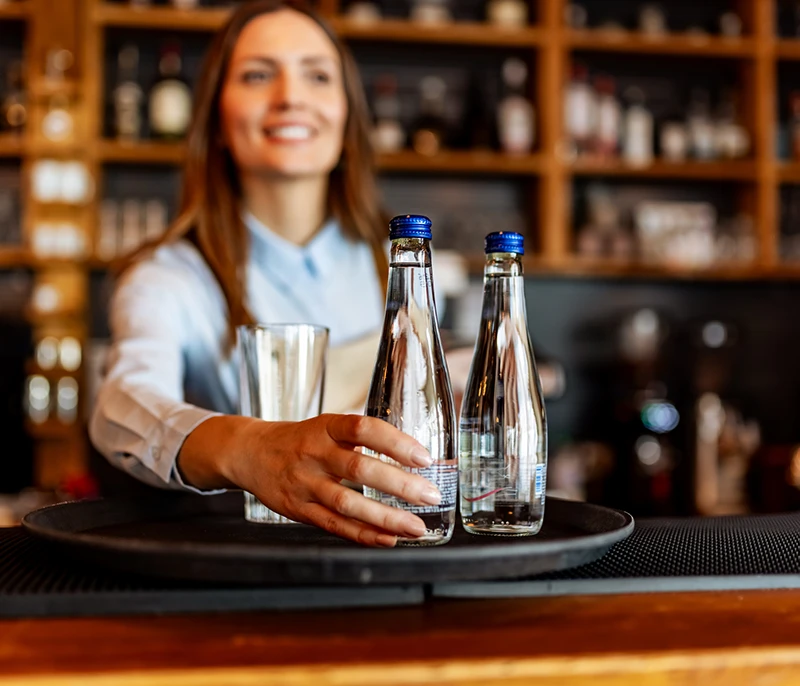 Hospitality employee serving bottled water and a glass on a tray