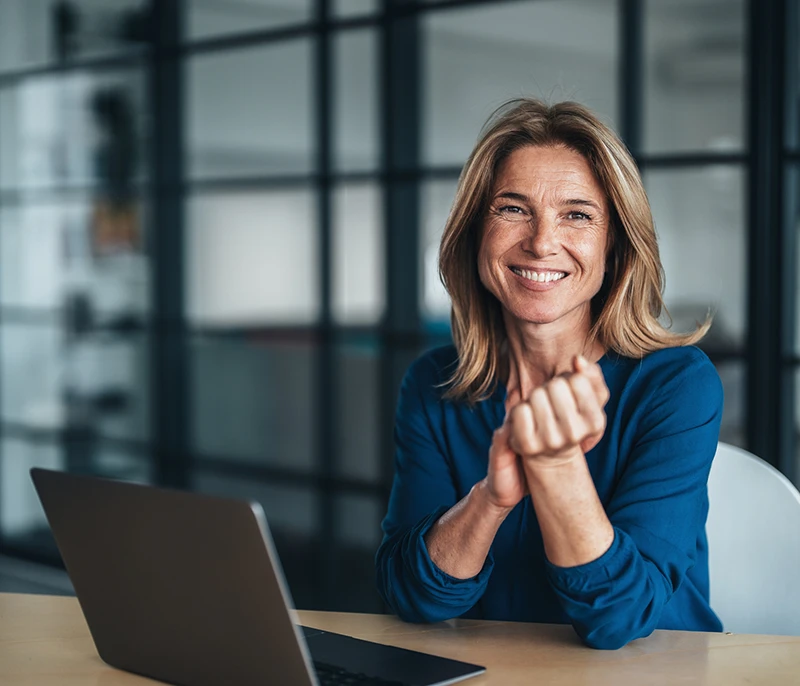 Business professional smiling while seated at a desk with a laptop