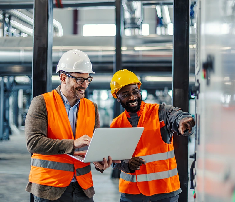 Two manufacturing professionals using a laptop while reviewing equipment on the factory floor