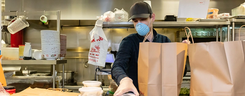 Restaurant employee wearing a face mask preparing takeout orders in a commercial kitchen