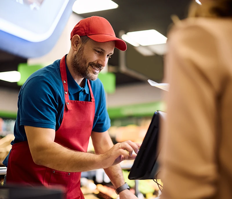 Frontline restaurant employee wearing a red apron and cap using a touchscreen register