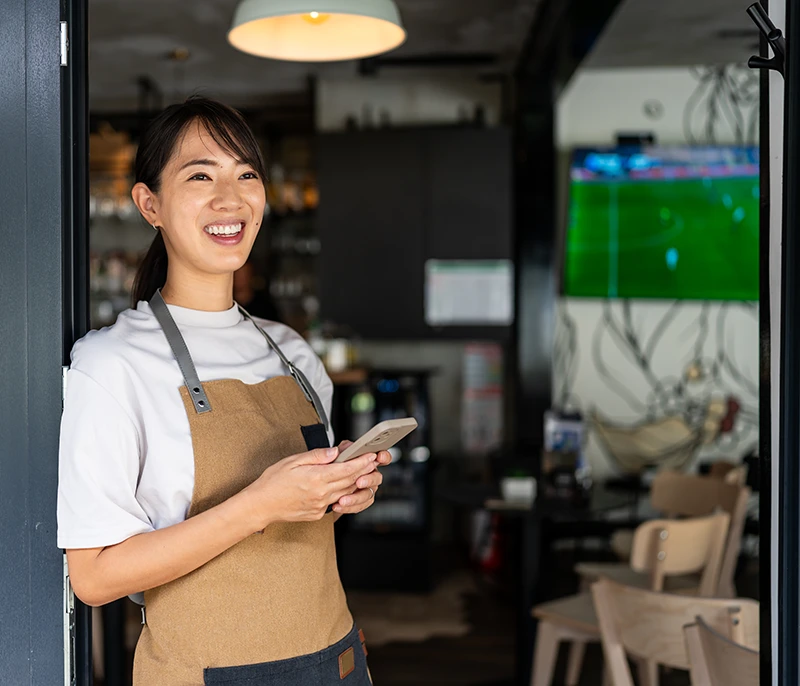 Smiling frontline restaurant employee wearing an apron and holding a smartphone
