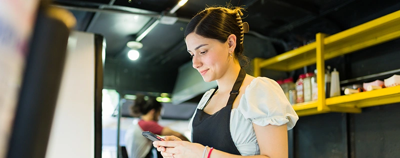 Restaurant employee wearing an apron and using a smartphone at work